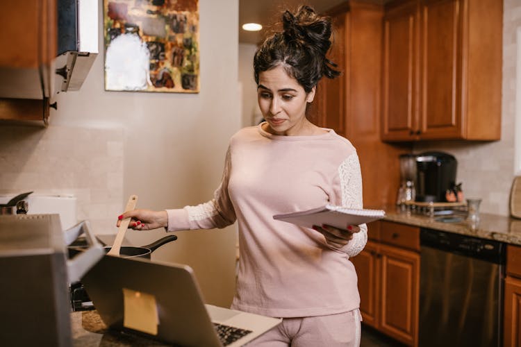 A Woman Cooking While Looking At Her Laptop