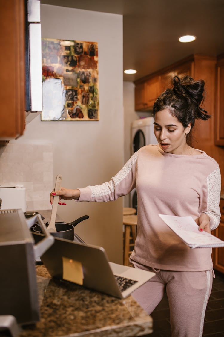 A Woman Cooking And Using A Laptop