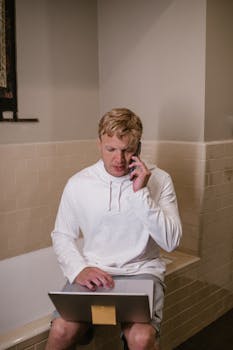 Young man multitasking on phone and laptop indoors, focused and busy.