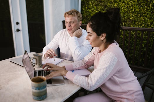 Two adults collaborating on laptops outdoors, working from home in a casual setting.