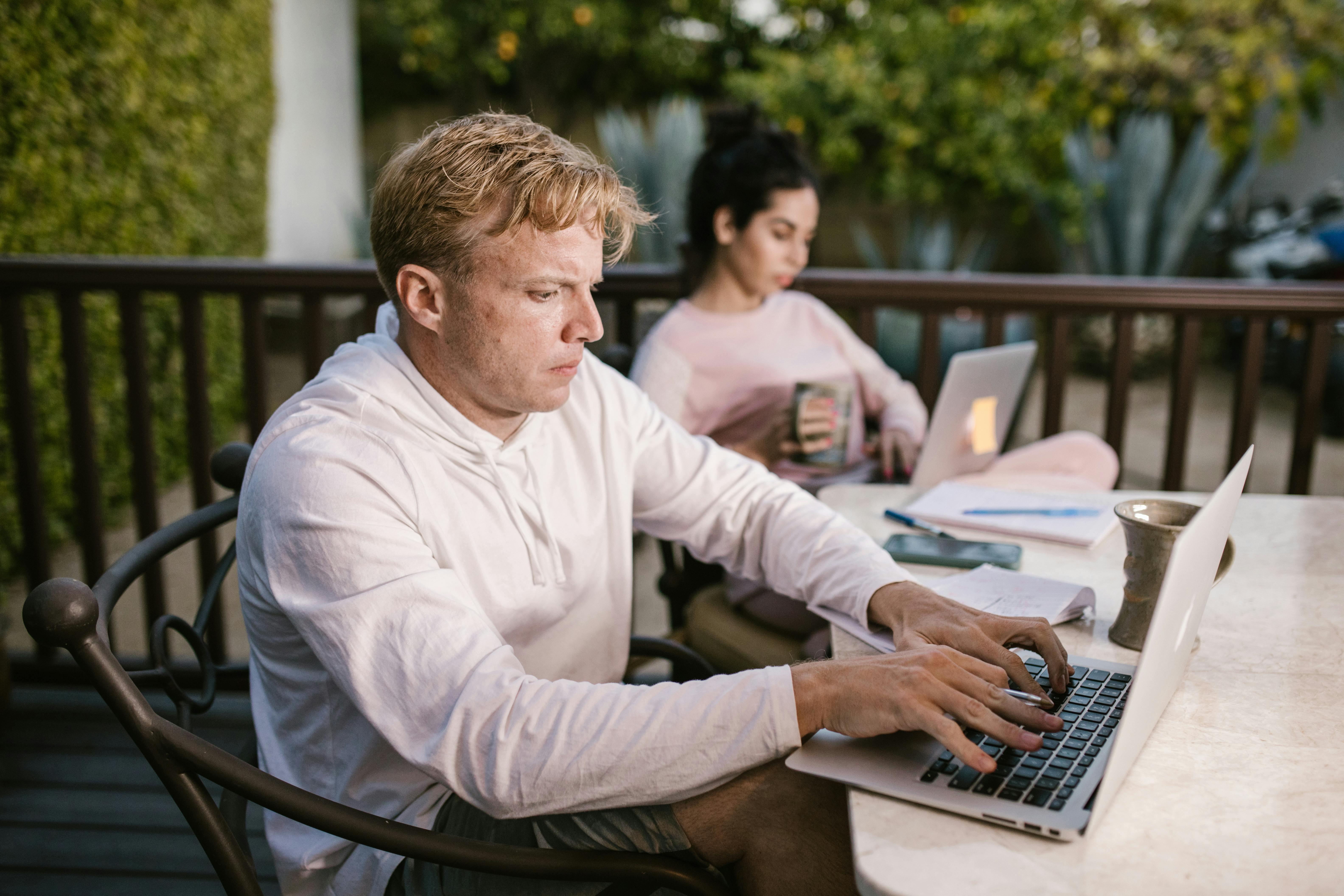 Man working on a laptop outdoors, focused on typing, while sitting on a patio.