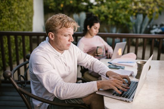 Man working on a laptop outdoors, focused on typing, while sitting on a patio.