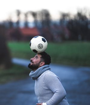 Side view of male football player balancing with ball on head during training in evening