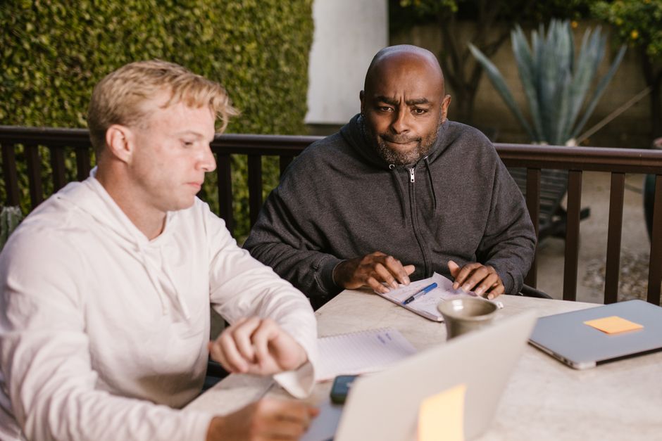 Two adults engaged in an outdoor meeting, using laptops and taking notes. Two adults engaged in an outdoor meeting, using laptops and taking notes.