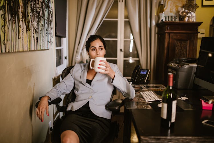 A Woman Holding A White Mug Near Her Computer