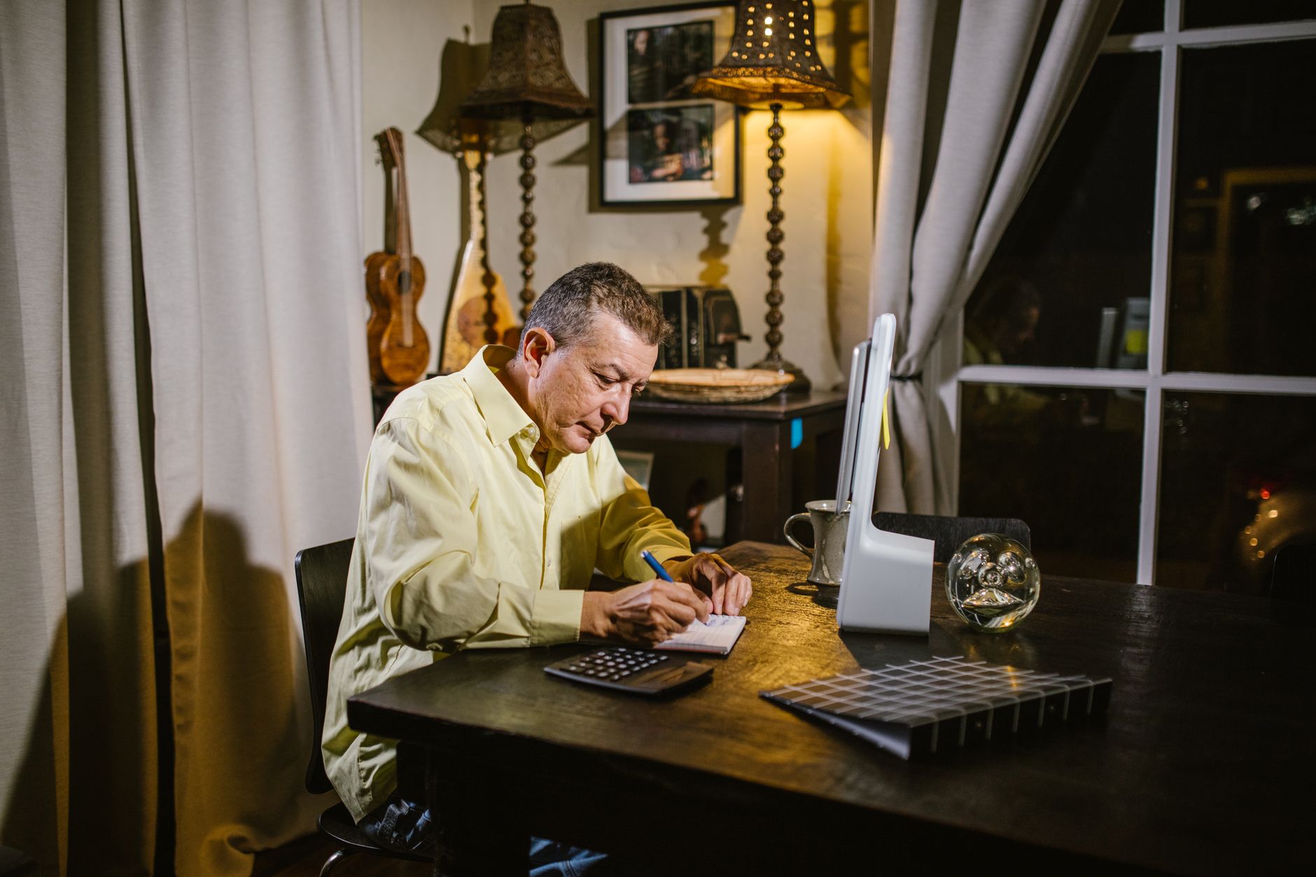 A person writing in a notebook at a kitchen table in the evening, the shape between-session homework takes
