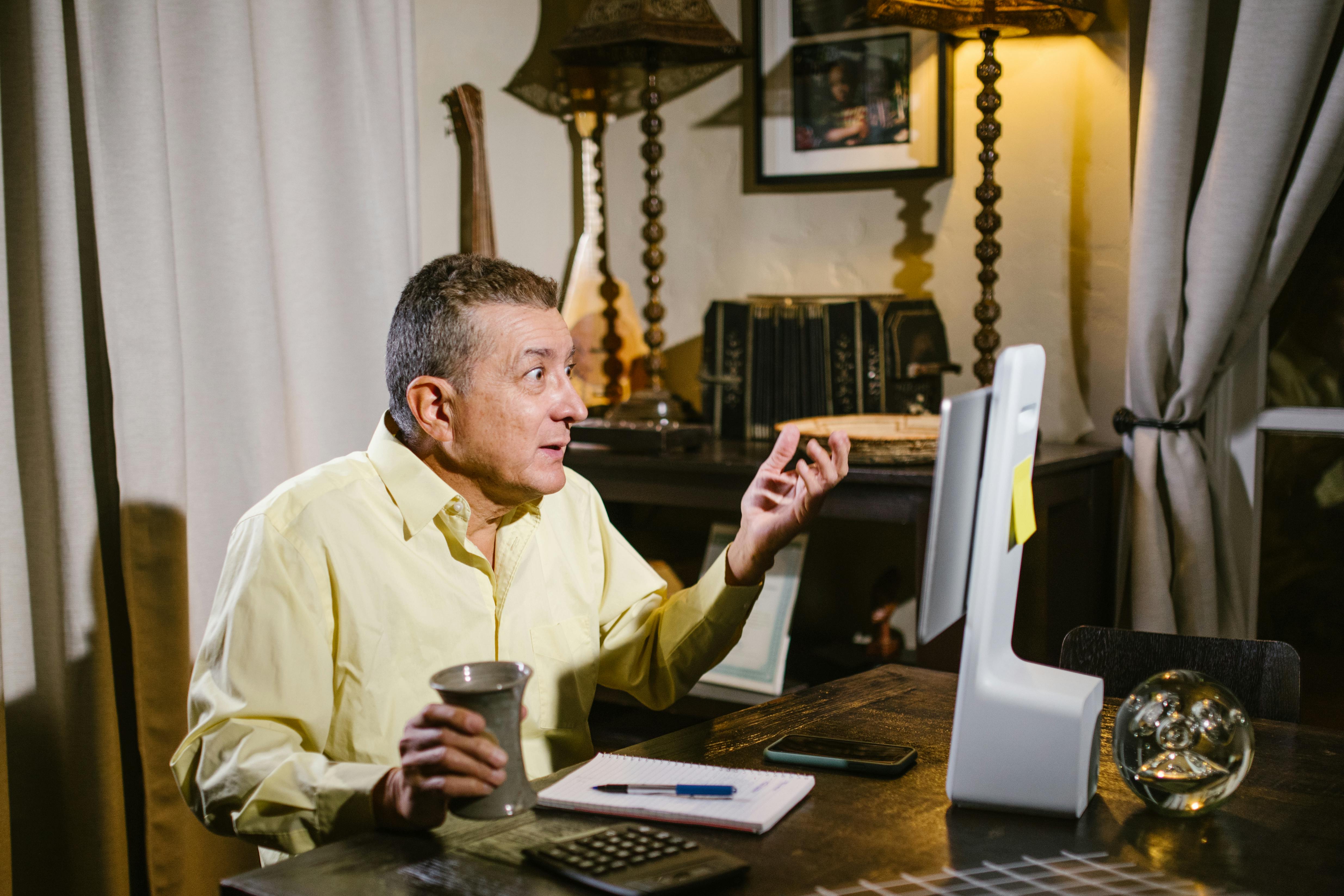 man wearing yellow dress shirt holding a cup looking at a computer screen