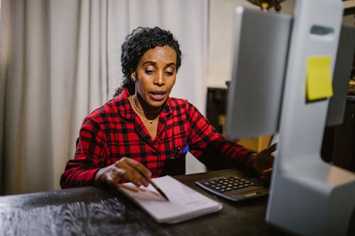 Free Woman Looking Down on Notebook in Front of a Computer Screen Stock Photo