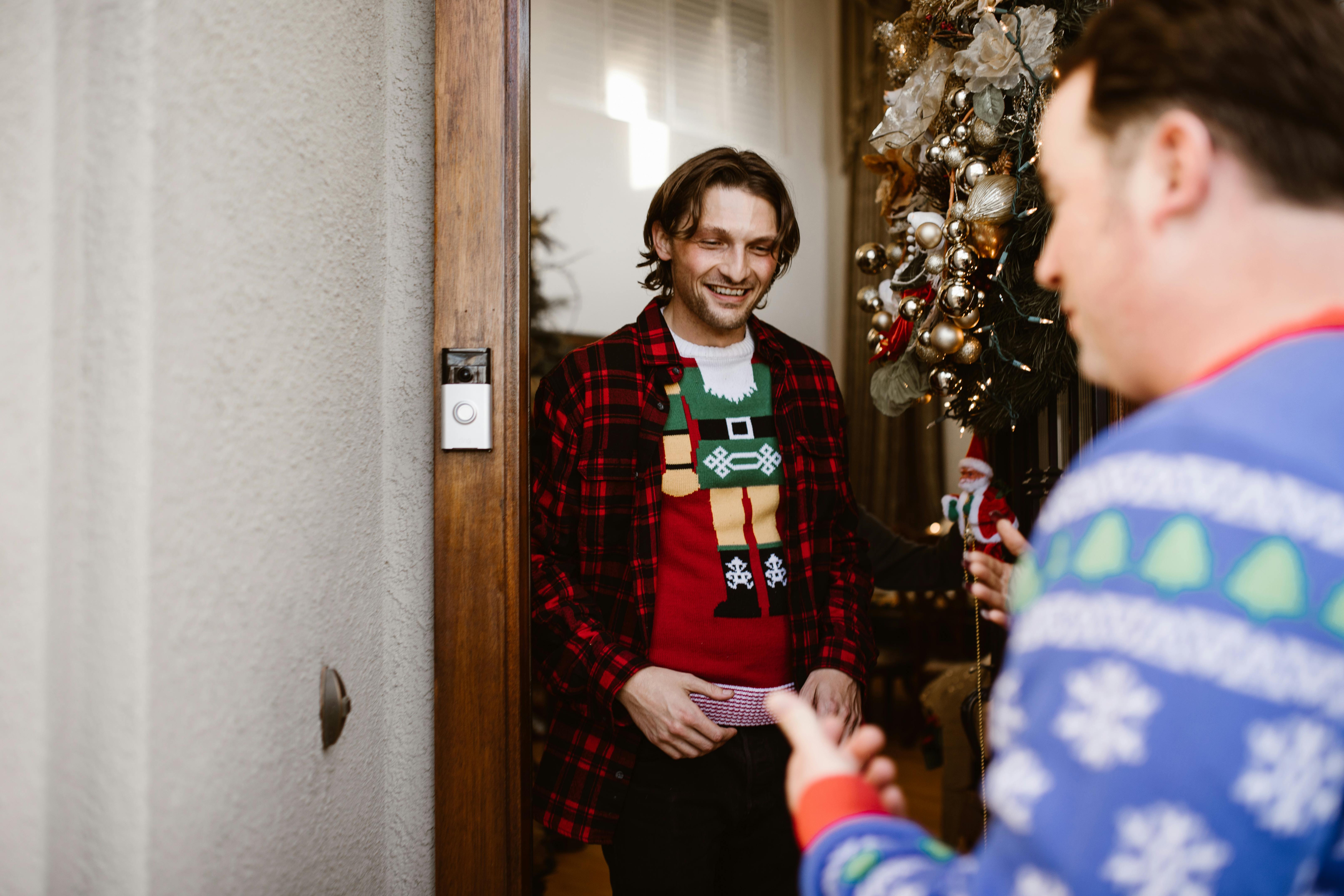 Two men enjoying a cheerful Christmas greeting in festive sweaters at a doorway.