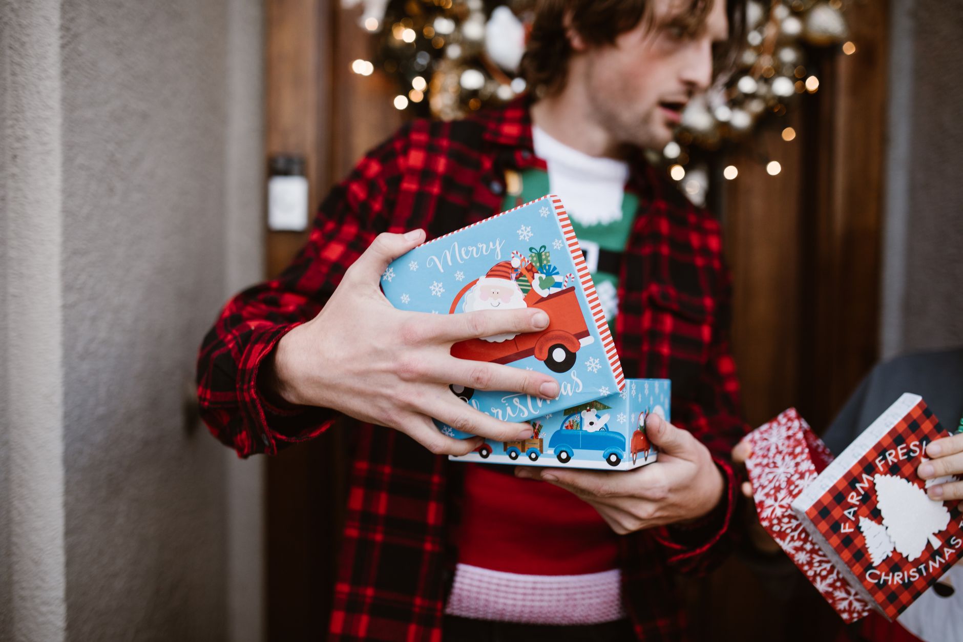 A man in a patterned shirt holds colorful Christmas presents outside, creating a festive holiday mood.