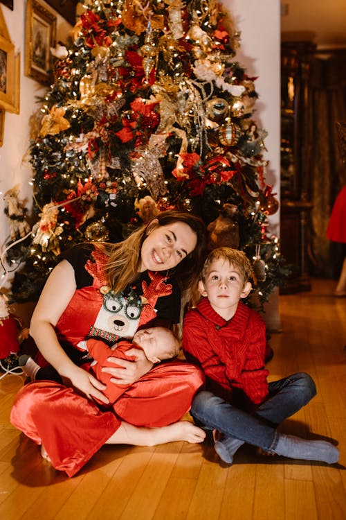 A Woman, a Boy and a Baby Sitting in Front of a Christmas Tree