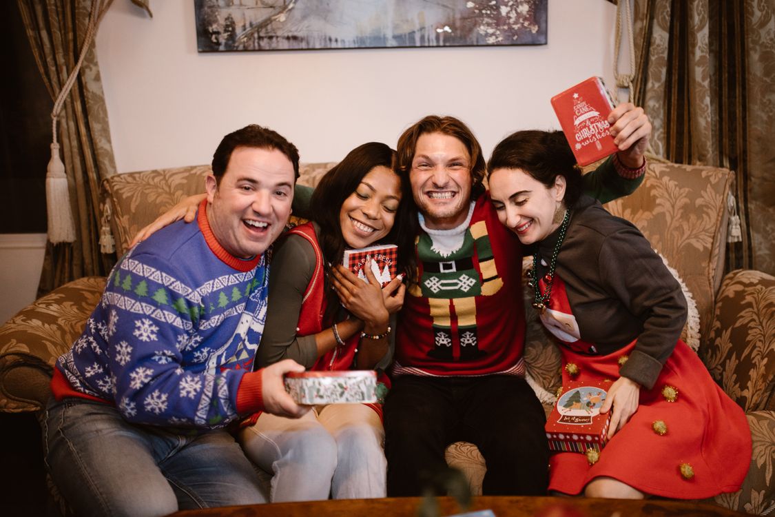Cheerful group of friends in festive sweaters sitting together holding wrapped gifts