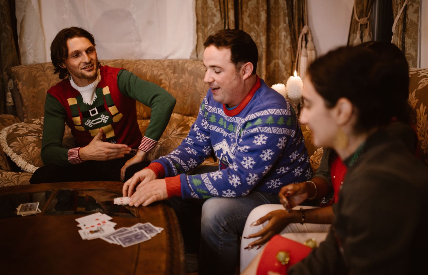 Friends enjoying a holiday card game wearing festive ugly sweaters indoors.