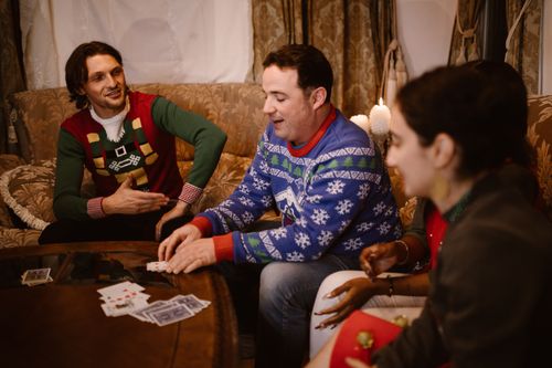 Free Friends enjoying a holiday card game wearing festive ugly sweaters indoors. Stock Photo