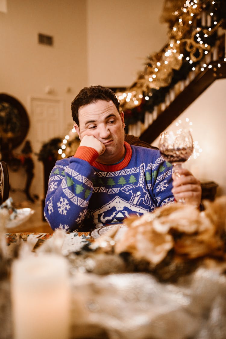 Man In Blue Christmas Sweater Holding A Glass Of Wine With Sad Face