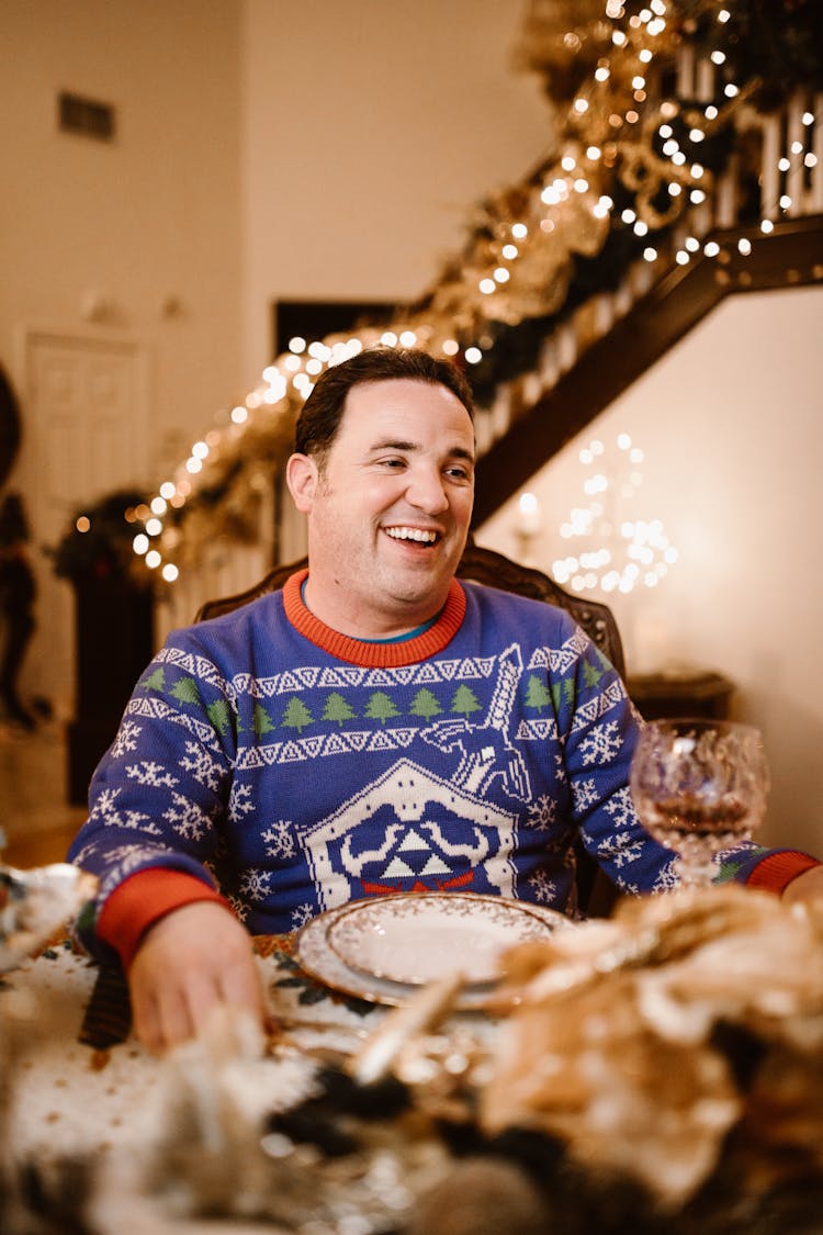 A Man In Blue Christmas Sweater Sitting At The Table