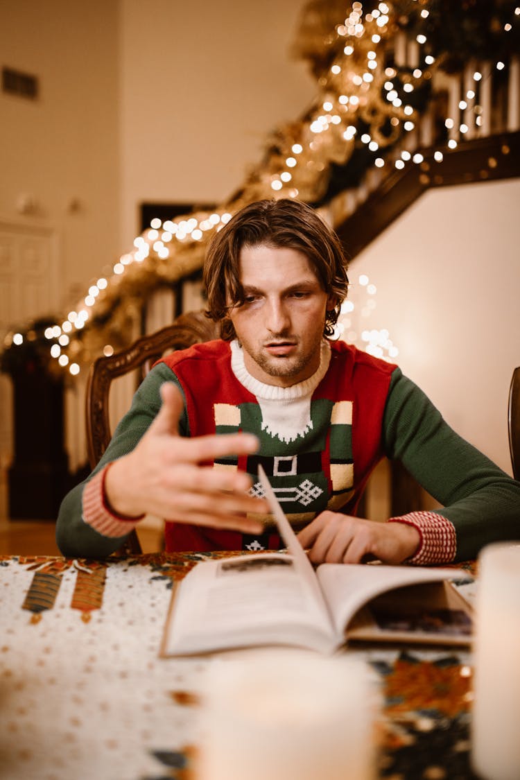 Man Wearing A Christmas Sweater Flipping Pages Of A Book