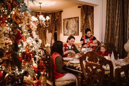 A joyful family gathered at home for a festive Christmas dinner with a beautifully decorated tree.