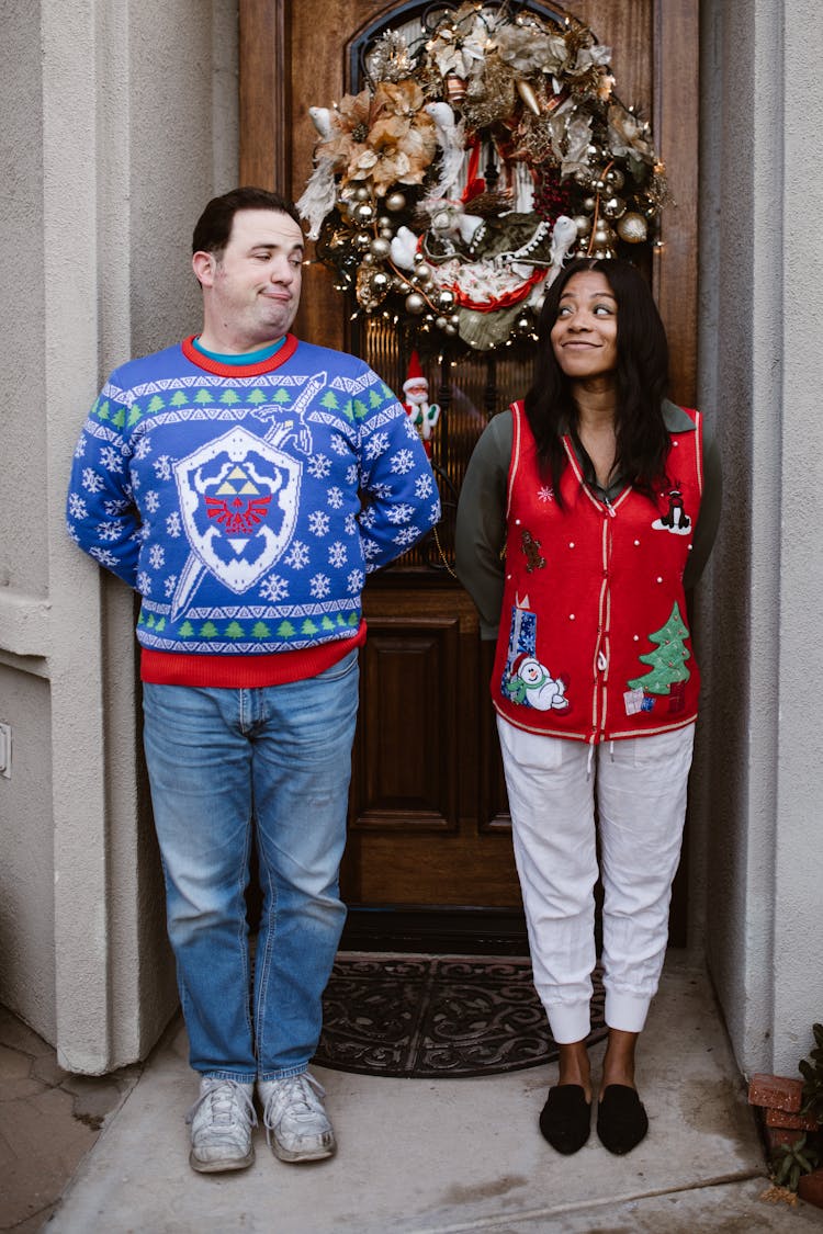 A Couple In Christmas Outfits Standing Near The Front Door