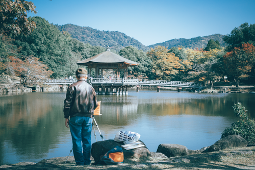 Free A serene moment captures a man painting by the lake with a gazebo and autumn foliage in the background. Stock Photo