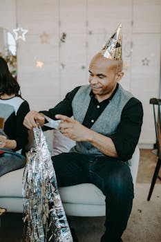 Man celebrating New Year indoors with party decor and hats, enjoying the festive atmosphere.