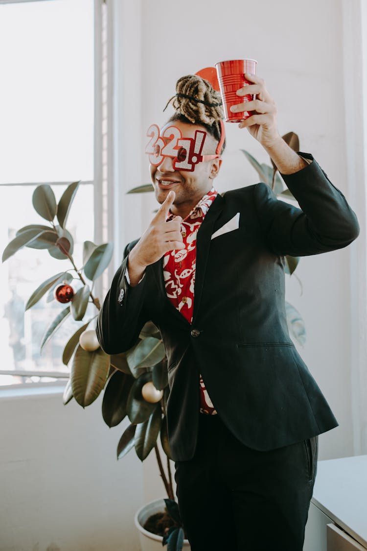 A Man In Black Suit Wearing 2021 Party Eye Mask Holding A Cup Of Drink