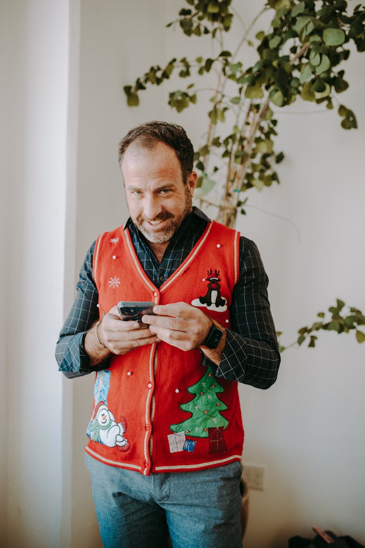 A Man Wearing Red Ugly Christmas Sweater Holding  A Cellphone