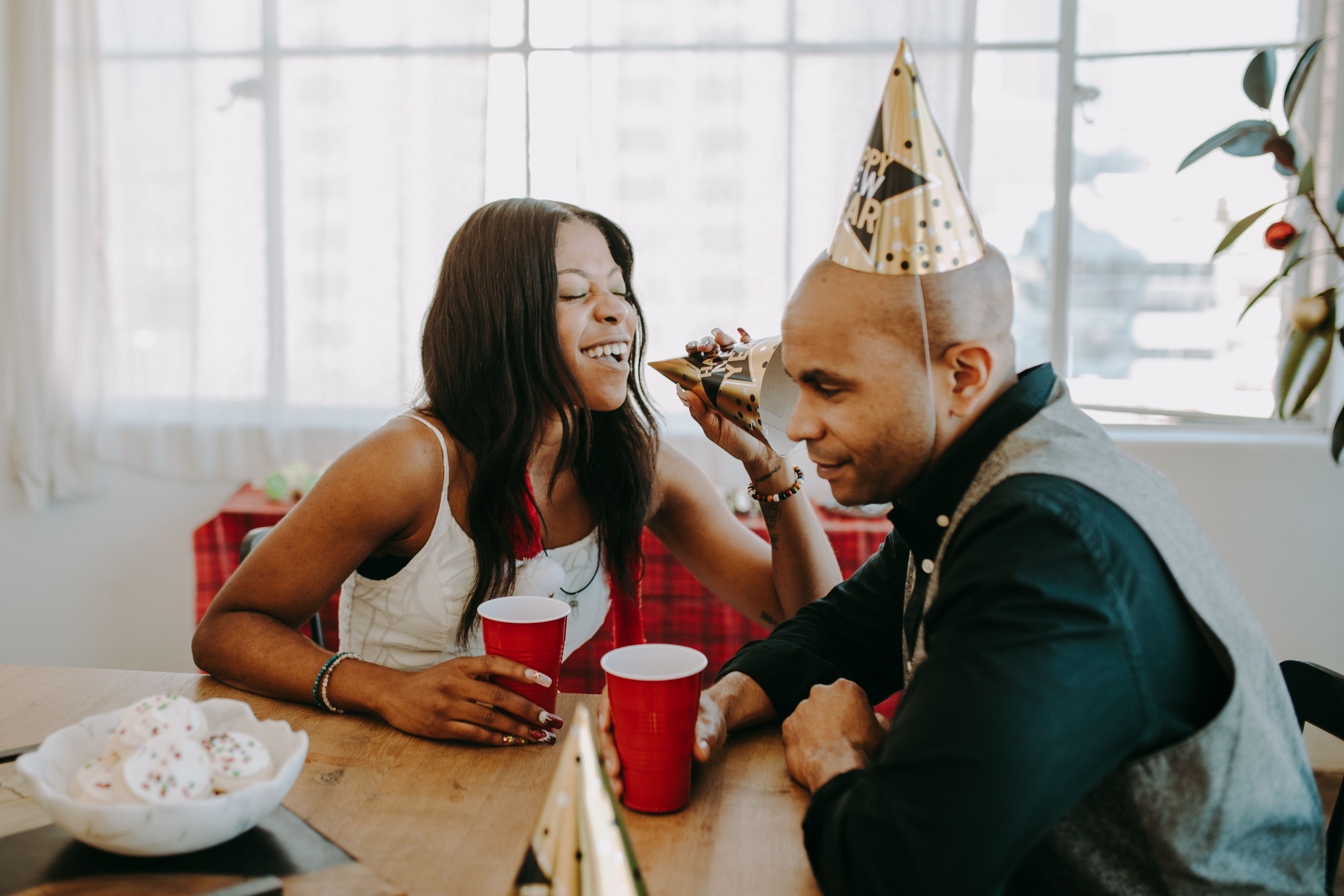 Two adults enjoy a New Year's party with drinks and laughter indoors.
