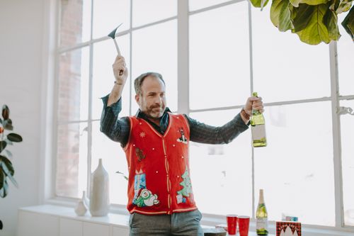 Free Man in a Christmas vest holding a bottle, surrounded by holiday decor indoors. Stock Photo