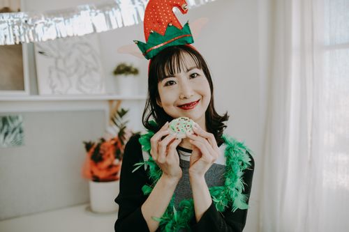 Free Smiling woman wearing elf hat holding a decorated Christmas cookie indoors. Stock Photo