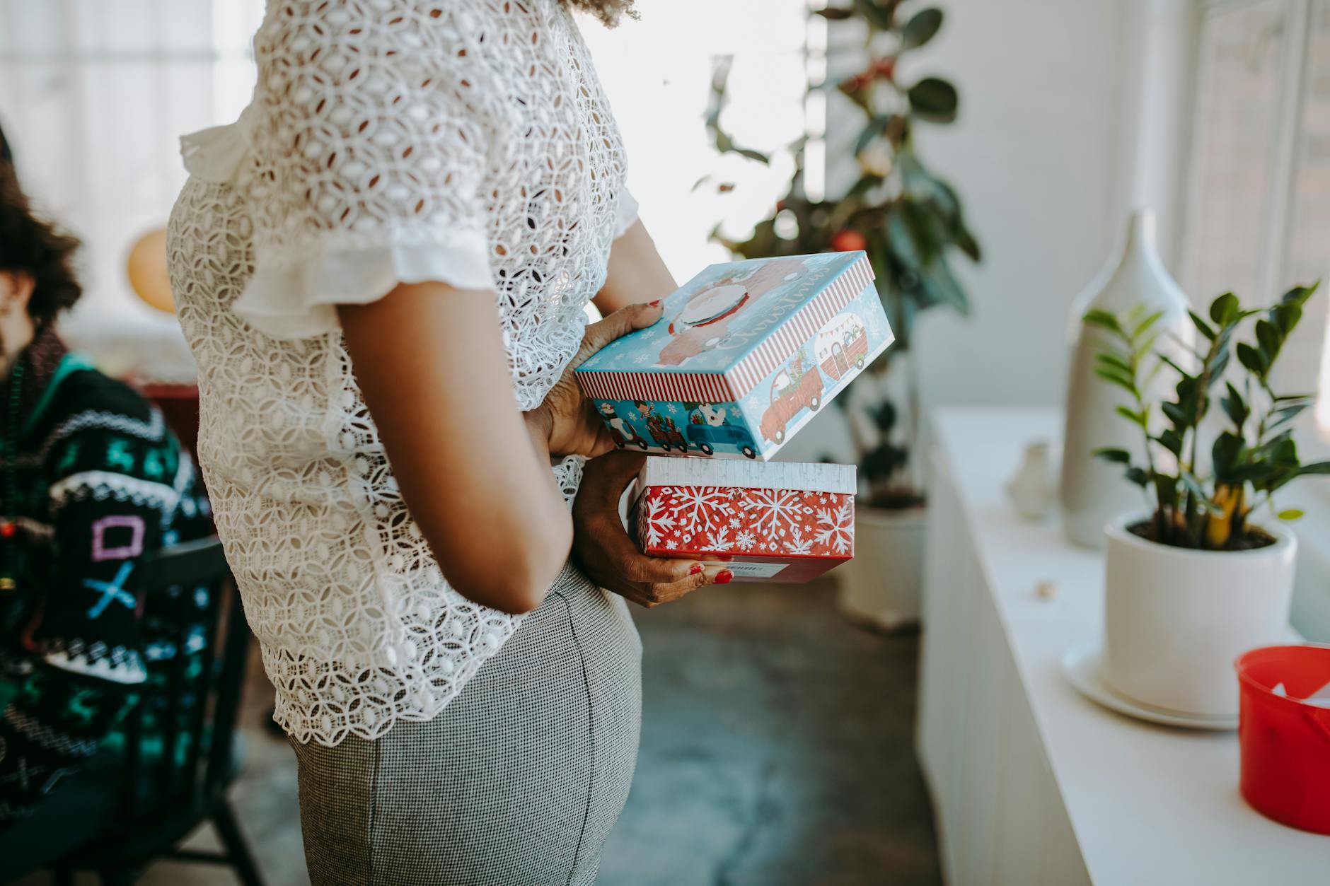 Woman holding Christmas gifts at a holiday gathering in a cozy indoor setting.