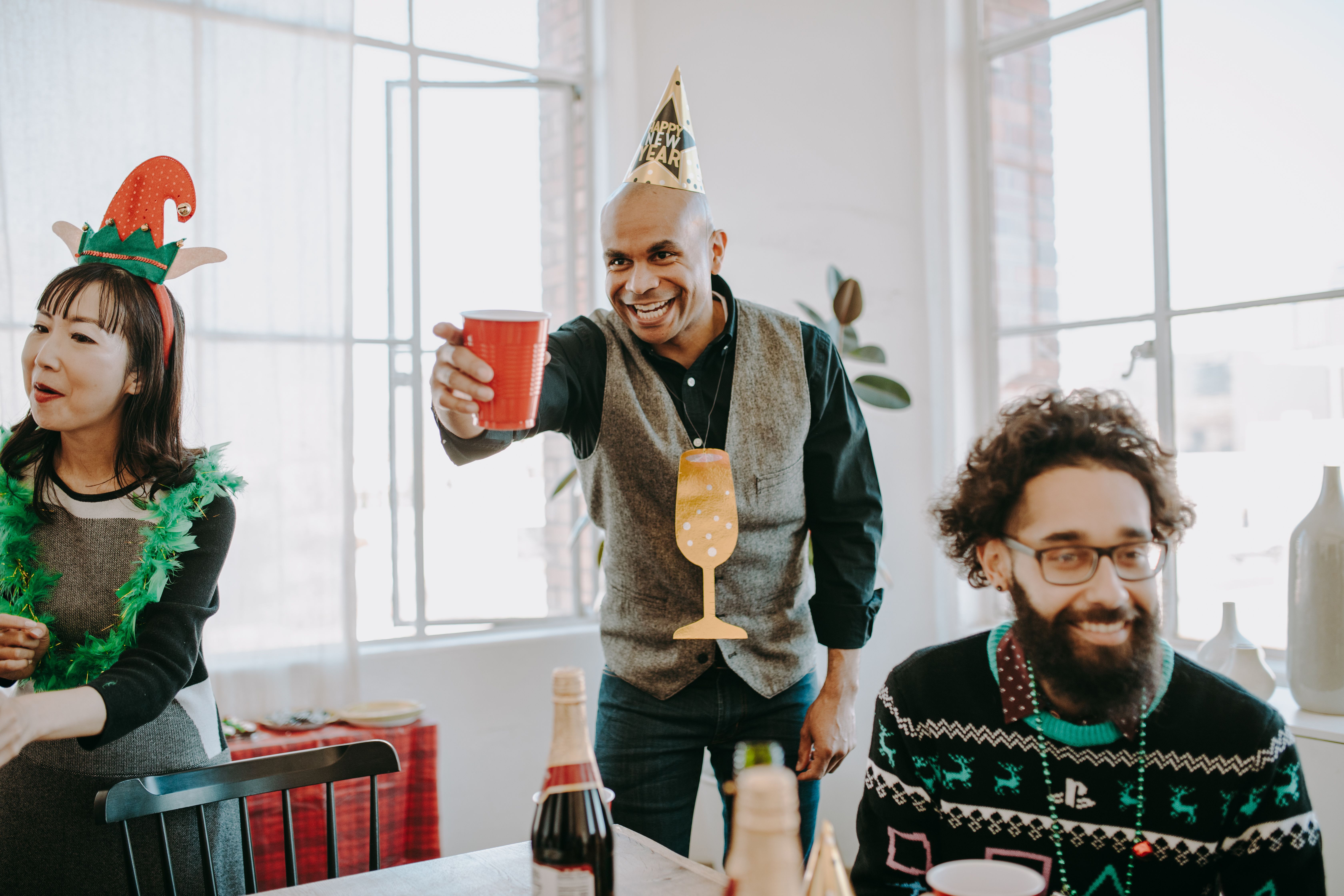 A group of diverse colleagues celebrating indoors with party hats and drinks at a festive event.