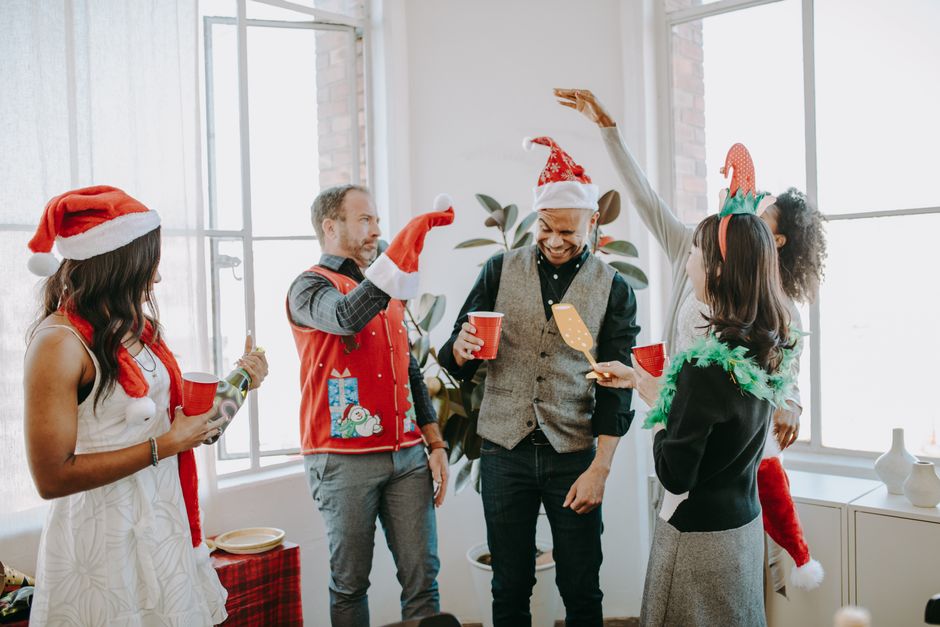 Group of diverse adults celebrating Christmas indoors with Santa hats and red cups.