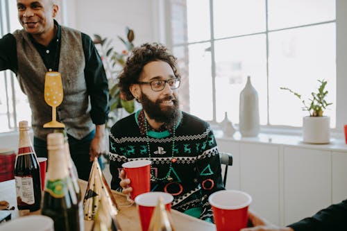 Free A Bearded Man in Ugly Sweater Talking while Holding a Red Cup Stock Photo