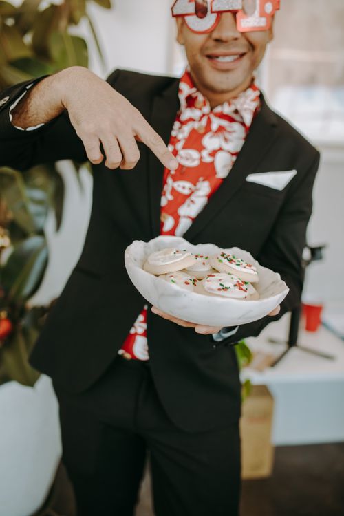 Free Man in suit pointing at bowl of decorated holiday cookies indoors. Stock Photo