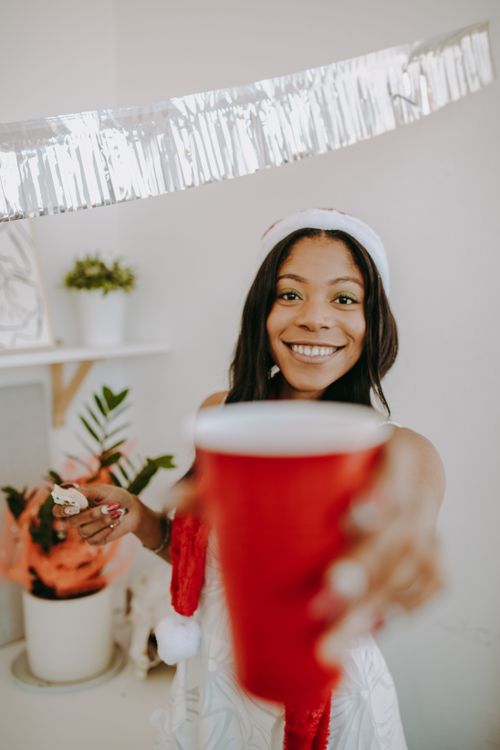 Free Smiling woman in Santa hat holding a red cup, celebrating indoors. Stock Photo