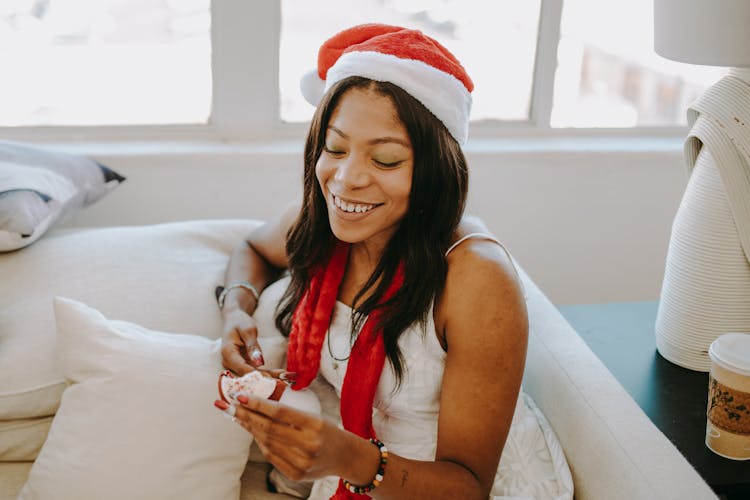 A Woman In Santa Hat Sitting On A Couch While Holding A Cookie