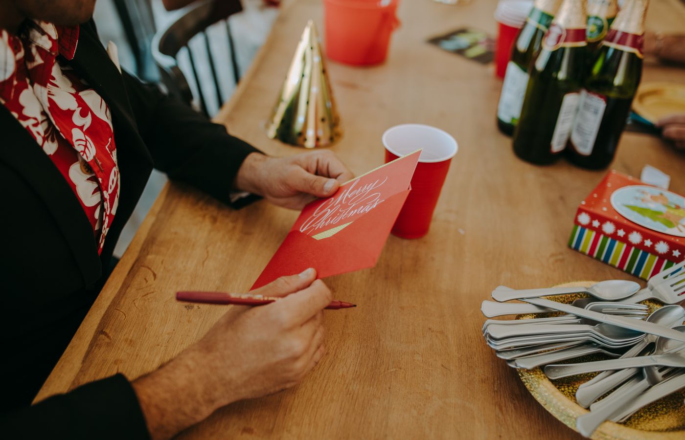 Man writing a Christmas card at a festive holiday party with drinks and decorations.