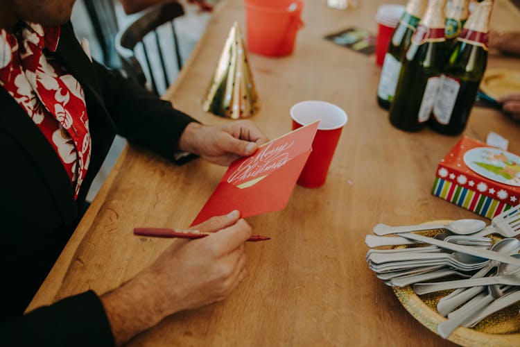 A Person In Black Long Sleeves Holding A Red Christmas Greeting Card