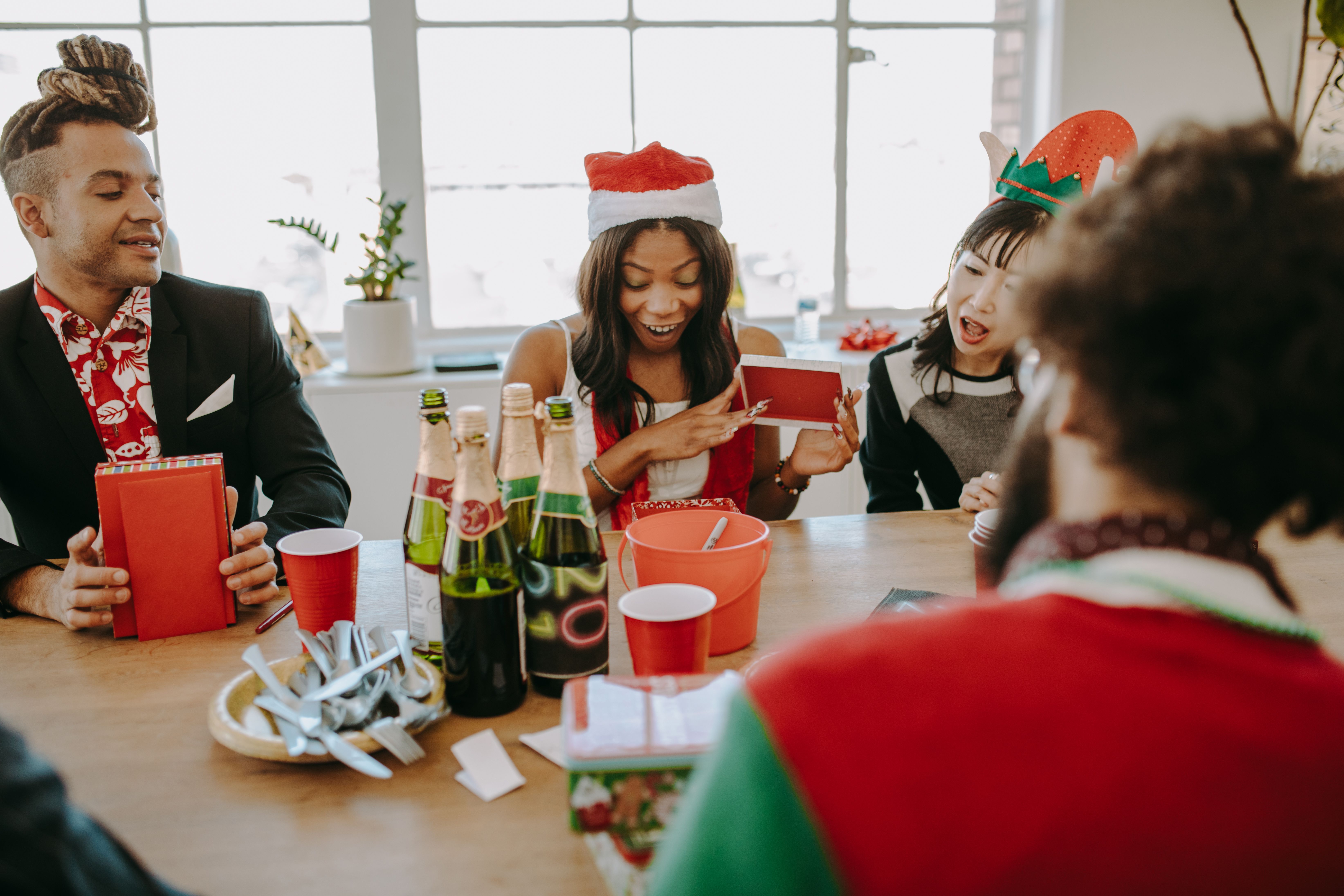 Diverse group of friends celebrating at a holiday party, exchanging gifts and enjoying drinks indoors.