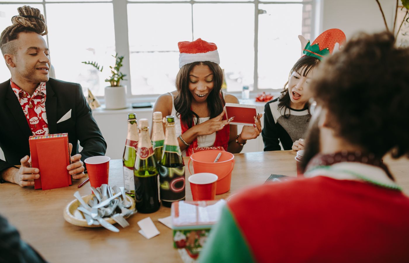 Diverse group of friends celebrating at a holiday party, exchanging gifts and enjoying drinks indoors.