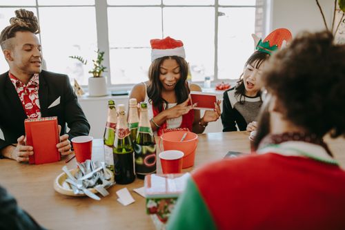 Free Diverse group of friends celebrating at a holiday party, exchanging gifts and enjoying drinks indoors. Stock Photo