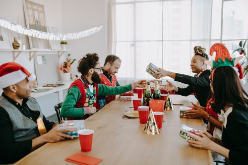 Free Diverse colleagues exchange gifts during a lively Christmas office party, celebrating the festive season with joy. Stock Photo
