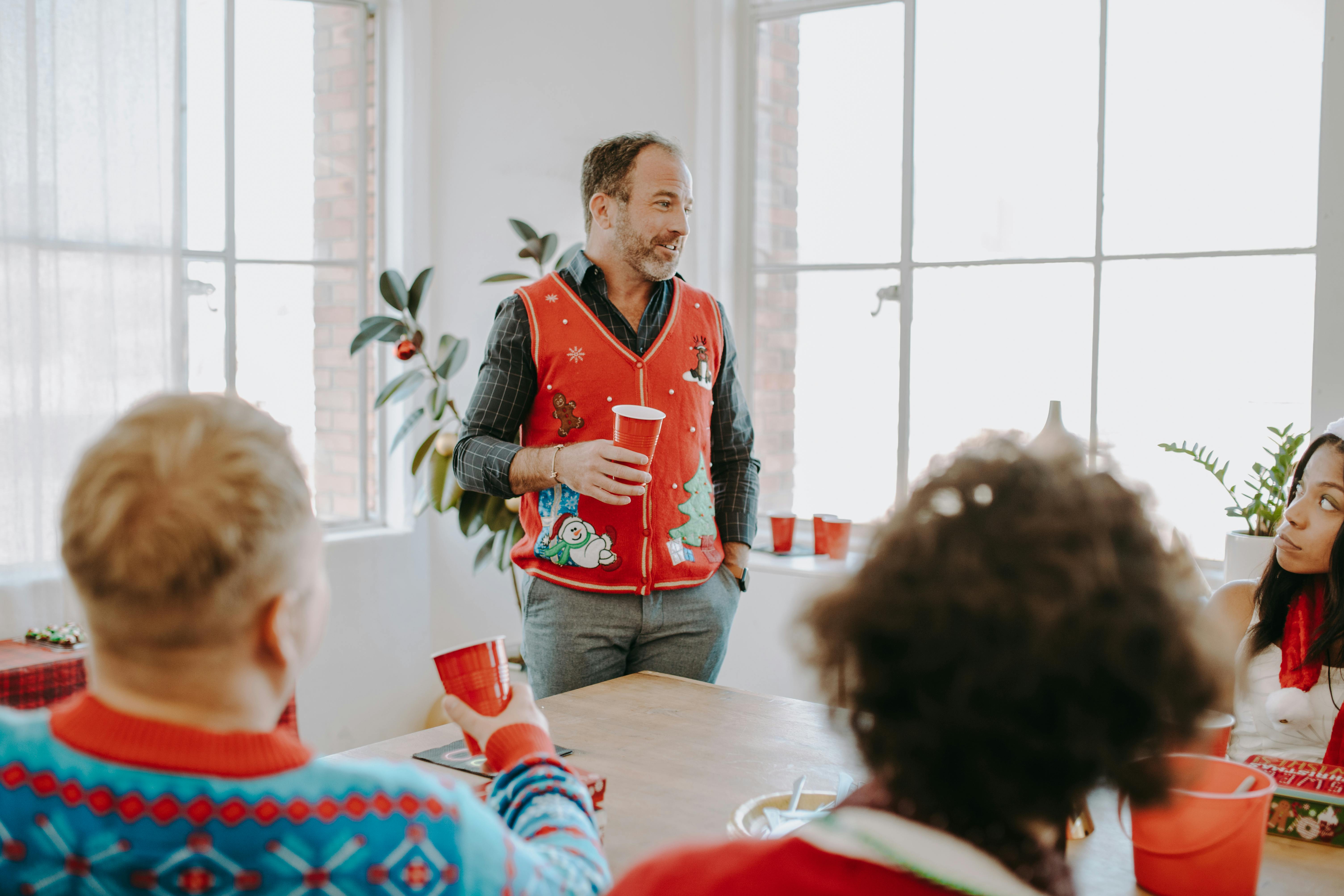Office Christmas party with adults in festive sweaters enjoying holiday gathering.