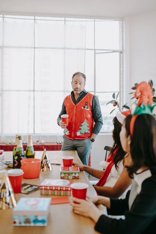 Free Casual office Christmas party with festive decorations and a man in a holiday vest holding a cup. Stock Photo