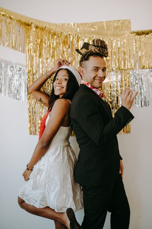 Free Cheerful couple in festive attire celebrating at a holiday party with golden decorations. Stock Photo