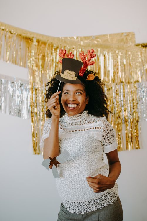 Free Smiling woman with reindeer antlers by festive gold decor at holiday party. Stock Photo