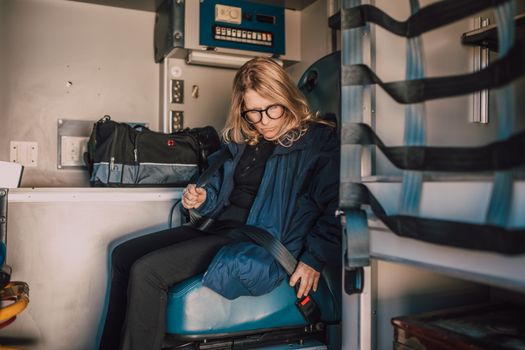 A woman seated and securing a seatbelt inside an ambulance, focused and prepared.