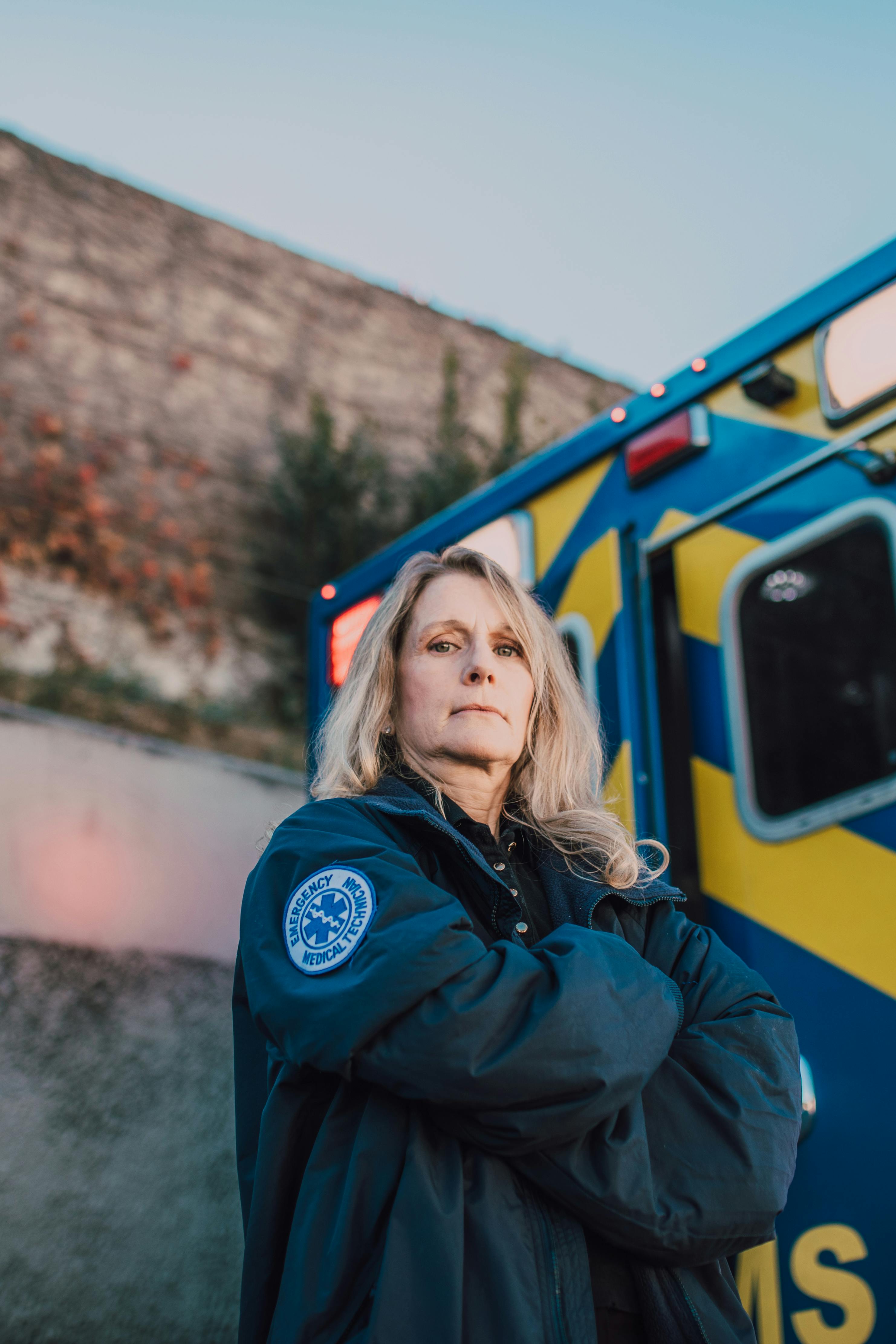A determined female paramedic stands confidently beside an EMS ambulance.