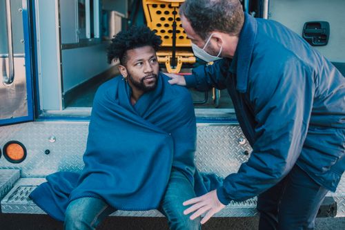 Free EMTs assist a man wrapped in a blanket near an ambulance, emphasizing care and response. Stock Photo